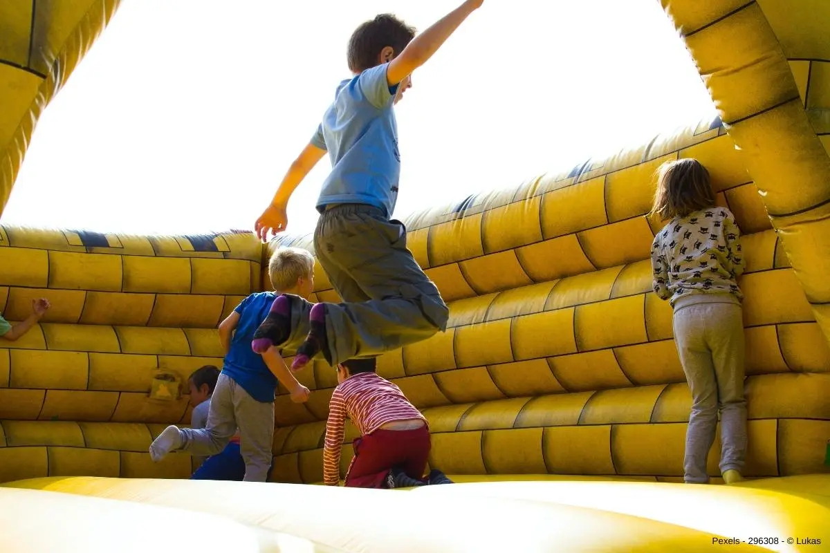 Kinder hüpfen auf gelber Hüpfburg - In diesem Beitrag erfahren Sie wissenswerte Infos darüber, wie Sie mit einer Hüpfburg eine Garten Party aufwerten.